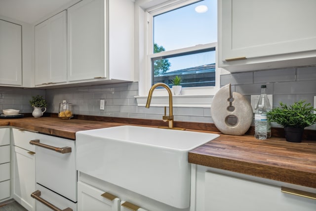 kitchen featuring butcher block countertops, sink, decorative backsplash, and white cabinetry