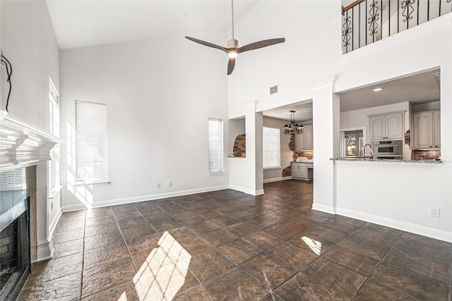 unfurnished living room with ceiling fan with notable chandelier, a high end fireplace, and high vaulted ceiling