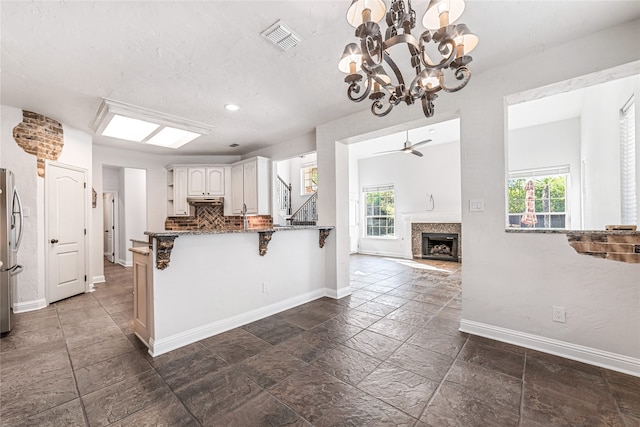 kitchen featuring tasteful backsplash, ceiling fan with notable chandelier, white cabinets, kitchen peninsula, and stainless steel refrigerator