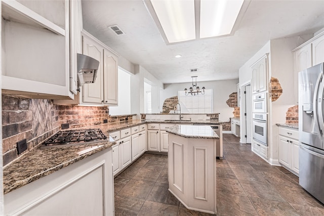 kitchen featuring sink, a kitchen island, appliances with stainless steel finishes, decorative light fixtures, and stone countertops