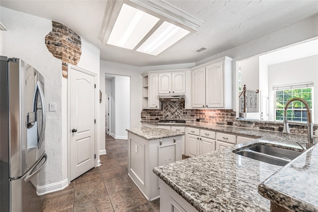 kitchen with light stone counters, sink, white cabinetry, a kitchen island, and stainless steel appliances