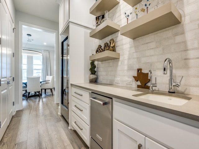 kitchen with decorative backsplash, white cabinetry, sink, and light hardwood / wood-style flooring