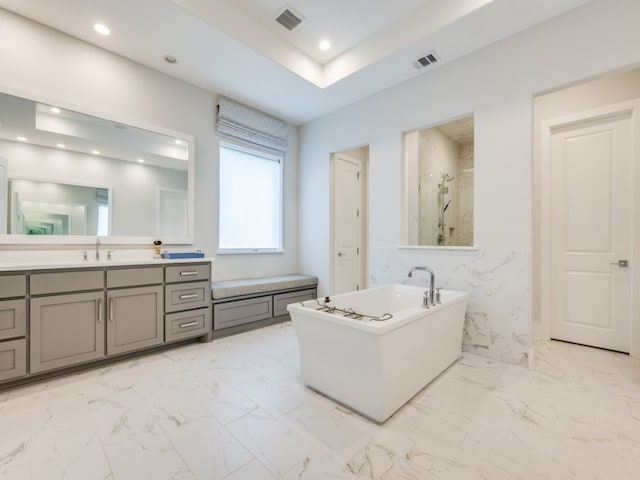 bathroom featuring independent shower and bath, vanity, and a raised ceiling