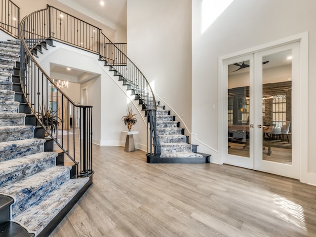 stairs with ceiling fan, hardwood / wood-style flooring, a towering ceiling, and french doors