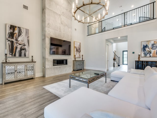 living room with a notable chandelier, light hardwood / wood-style floors, a premium fireplace, and a high ceiling