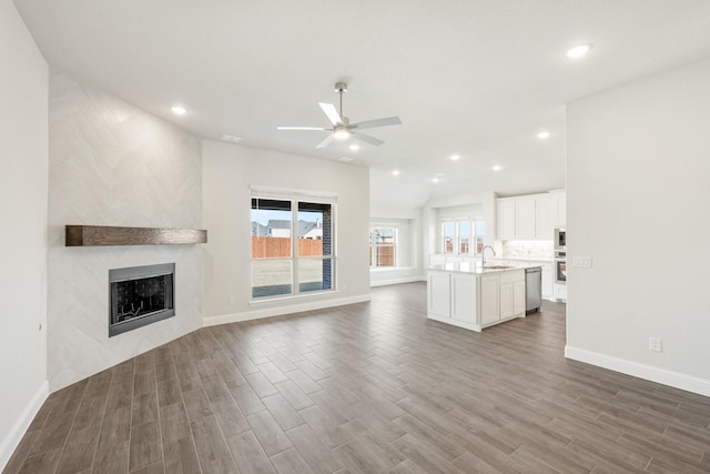 unfurnished living room featuring ceiling fan, a fireplace, sink, and dark hardwood / wood-style floors