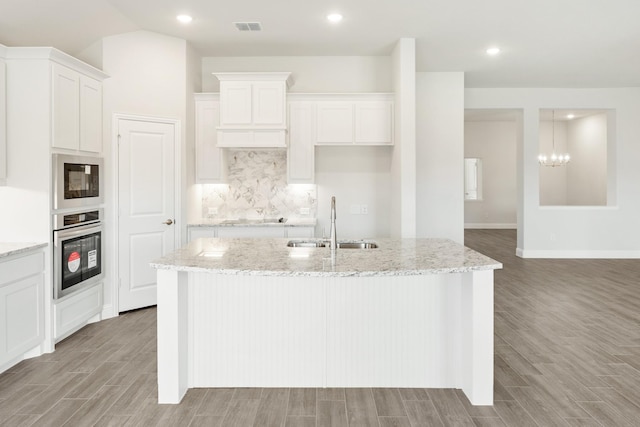 kitchen with white cabinetry, sink, an island with sink, and oven