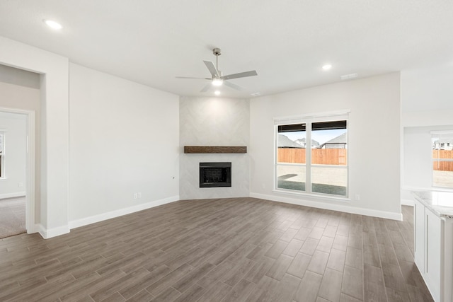 unfurnished living room featuring dark wood-type flooring, a large fireplace, and ceiling fan