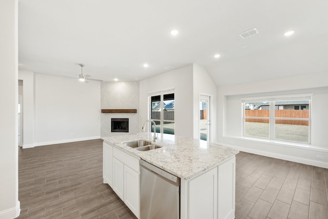 kitchen featuring a center island with sink, dishwasher, light stone countertops, white cabinets, and sink