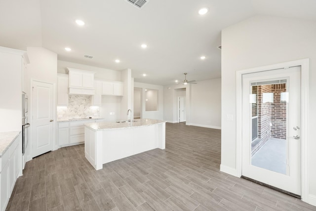 kitchen with a kitchen island with sink, sink, white cabinetry, and light stone counters