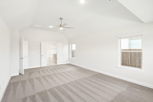 interior space featuring vaulted ceiling, ensuite bathroom, light carpet, and multiple windows