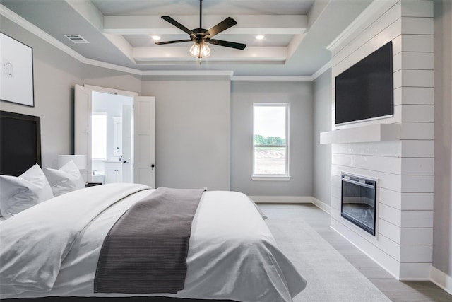 bedroom with a tray ceiling, ornamental molding, a large fireplace, and ceiling fan