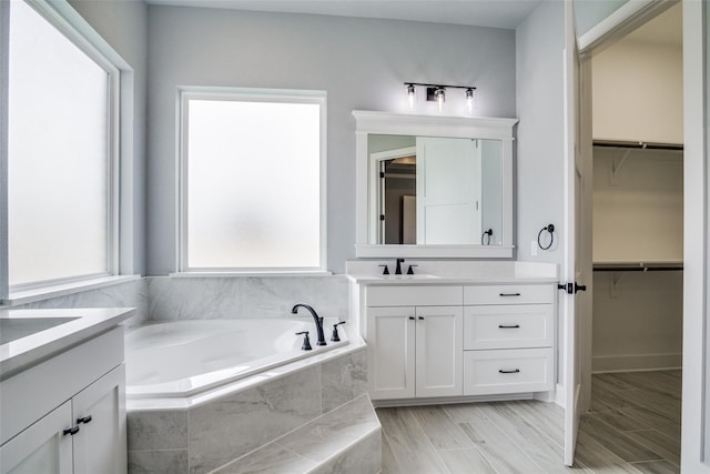 bathroom with a relaxing tiled tub, hardwood / wood-style floors, and vanity