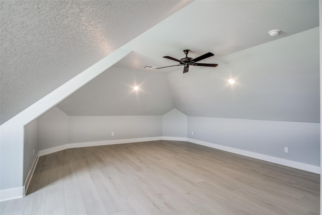 bonus room with light wood-type flooring, lofted ceiling, ceiling fan, and a textured ceiling