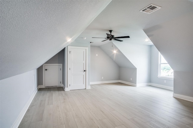 bonus room with light wood-type flooring, a textured ceiling, lofted ceiling, and ceiling fan