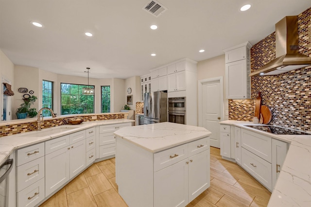 kitchen featuring white cabinets, wall chimney exhaust hood, decorative light fixtures, and appliances with stainless steel finishes