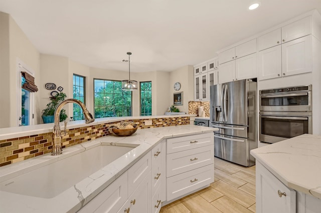 kitchen with sink, stainless steel appliances, tasteful backsplash, pendant lighting, and white cabinets