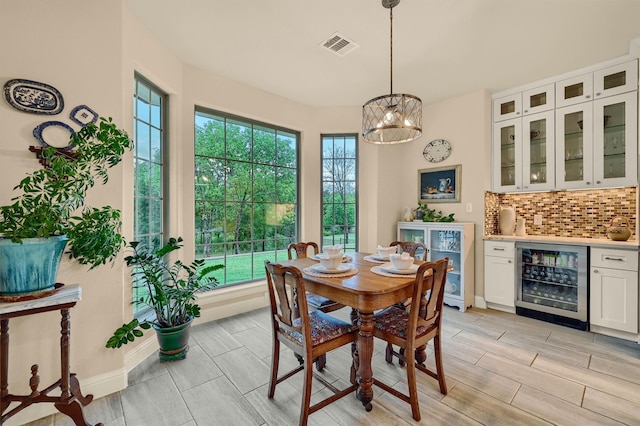 dining room with light wood-type flooring, wine cooler, and a chandelier