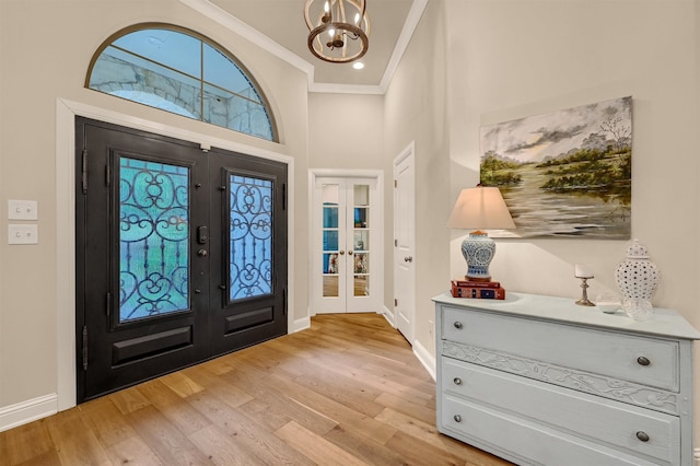 foyer featuring french doors, light wood-type flooring, ornamental molding, an inviting chandelier, and a high ceiling