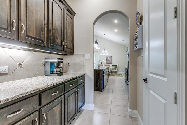 kitchen with dark brown cabinetry, light tile patterned floors, decorative backsplash, sink, and lofted ceiling