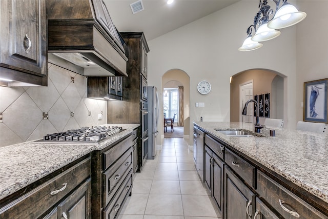 kitchen with dark brown cabinetry, sink, custom range hood, light tile patterned flooring, and appliances with stainless steel finishes