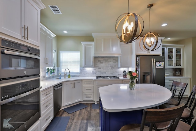 kitchen featuring appliances with stainless steel finishes, dark wood-type flooring, white cabinets, pendant lighting, and a notable chandelier