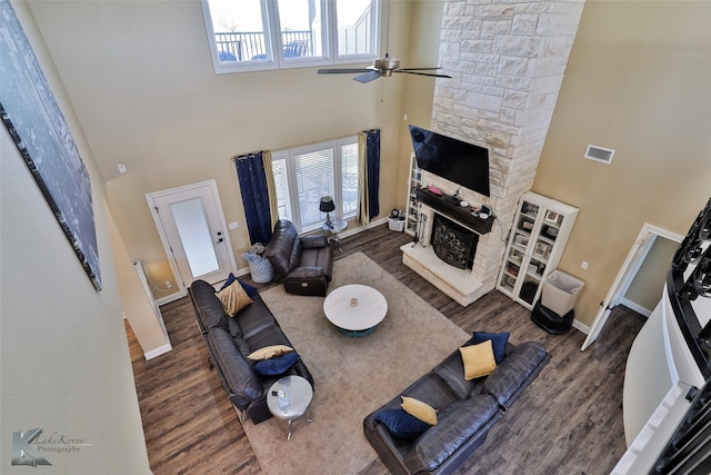 living room with a high ceiling, ceiling fan, dark wood-type flooring, and a stone fireplace