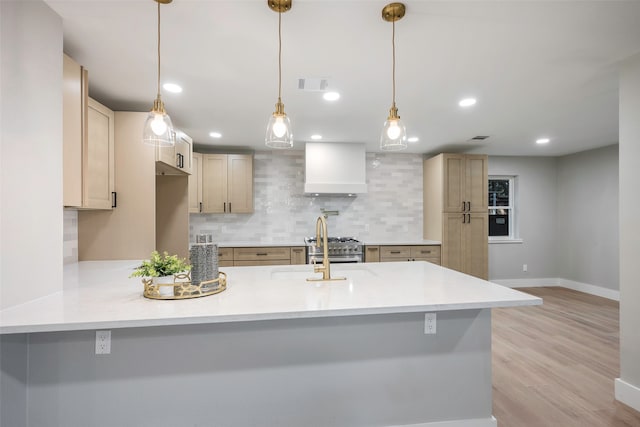 kitchen with sink, tasteful backsplash, custom exhaust hood, pendant lighting, and light hardwood / wood-style flooring