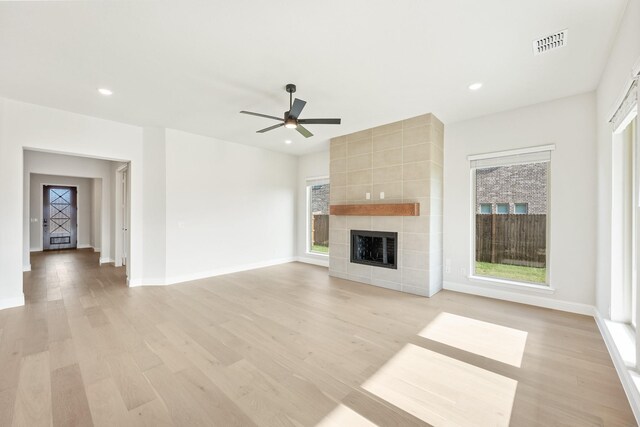 unfurnished living room with a tiled fireplace, ceiling fan, and light hardwood / wood-style flooring