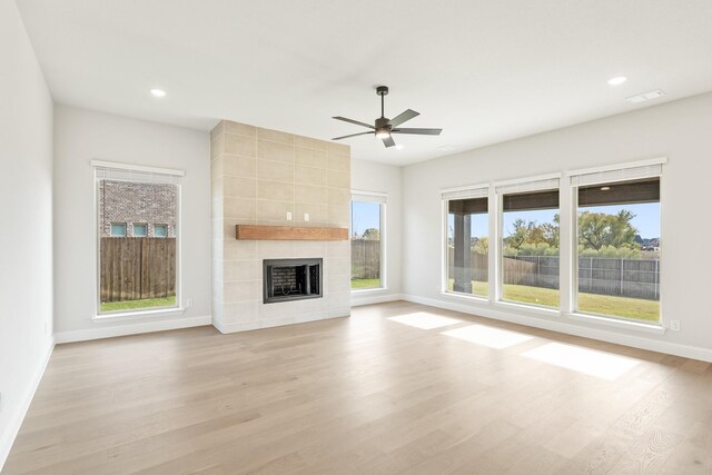 unfurnished living room with a wealth of natural light, a fireplace, ceiling fan, and light wood-type flooring