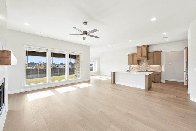 unfurnished living room featuring ceiling fan, sink, and light wood-type flooring