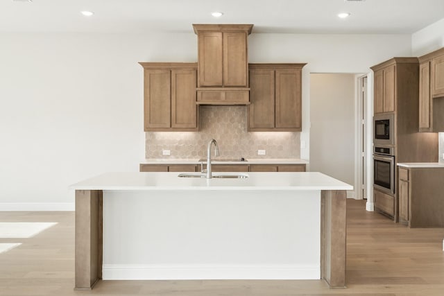 kitchen featuring a center island with sink, oven, built in microwave, and light hardwood / wood-style floors