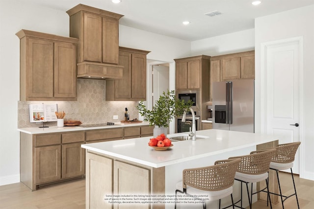 kitchen with custom exhaust hood, a center island with sink, sink, light wood-type flooring, and appliances with stainless steel finishes