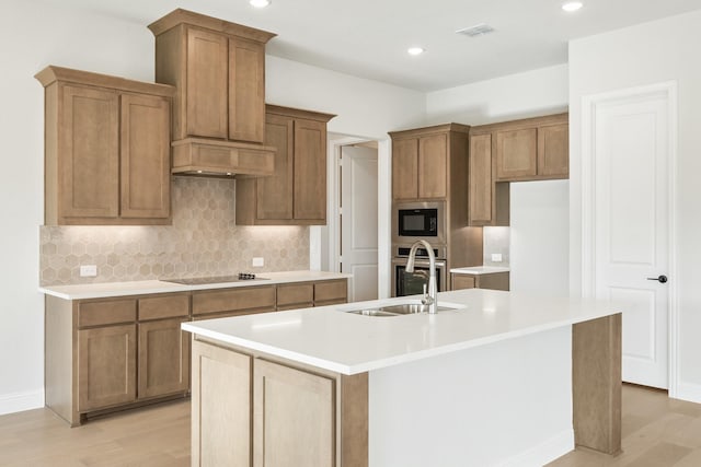 kitchen with black electric stovetop, light wood-type flooring, backsplash, built in microwave, and an island with sink