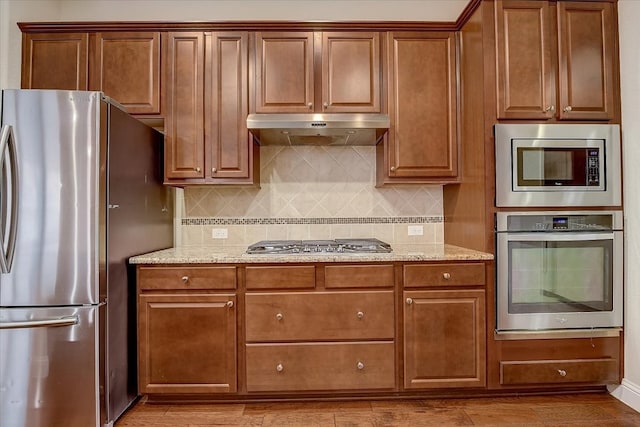 kitchen with light wood-type flooring, backsplash, stainless steel appliances, and light stone counters