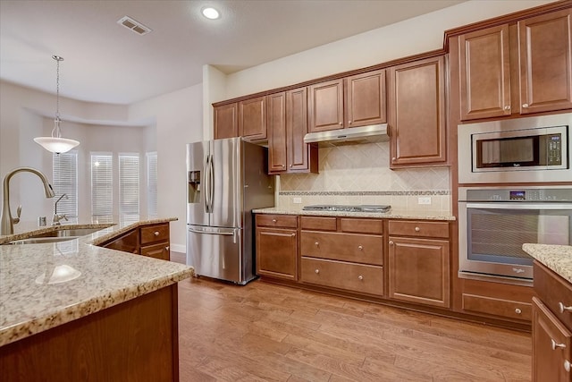 kitchen with light wood-type flooring, light stone counters, sink, appliances with stainless steel finishes, and decorative light fixtures