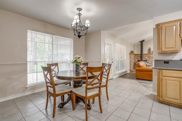 dining area with light tile patterned flooring, lofted ceiling, a notable chandelier, and a wood stove