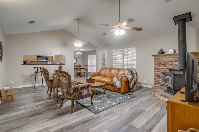 living room with light hardwood / wood-style flooring, a wood stove, vaulted ceiling, and ceiling fan