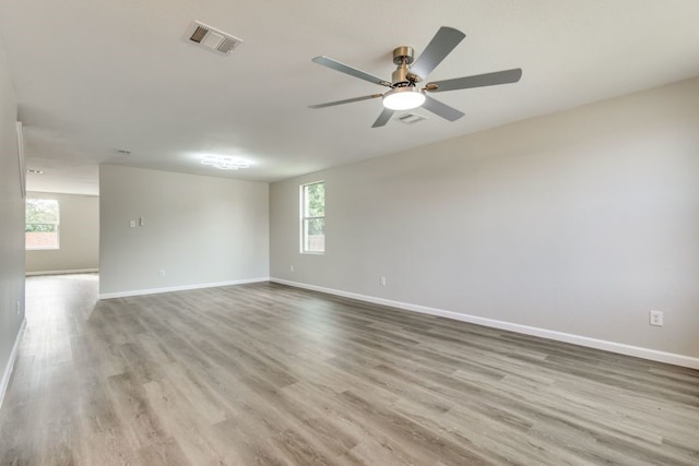 empty room featuring a wealth of natural light, ceiling fan, and light wood-type flooring