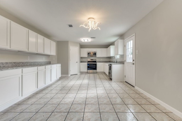 kitchen featuring sink, white cabinets, appliances with stainless steel finishes, light tile patterned floors, and light stone countertops