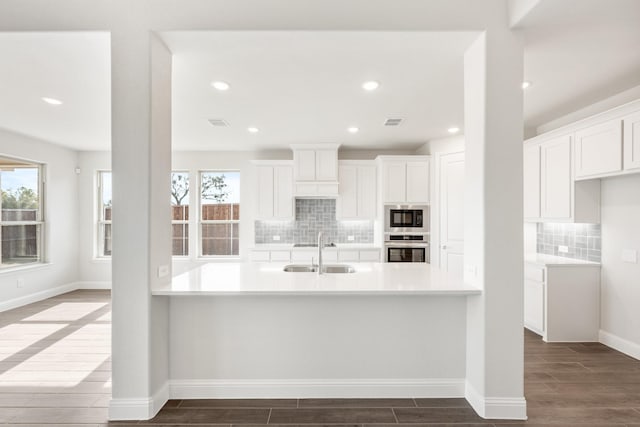 kitchen with built in microwave, sink, white cabinetry, kitchen peninsula, and oven