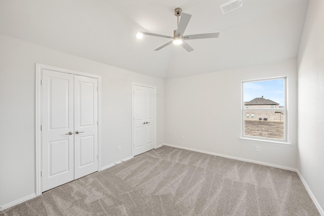 unfurnished bedroom featuring light carpet, two closets, lofted ceiling, and ceiling fan