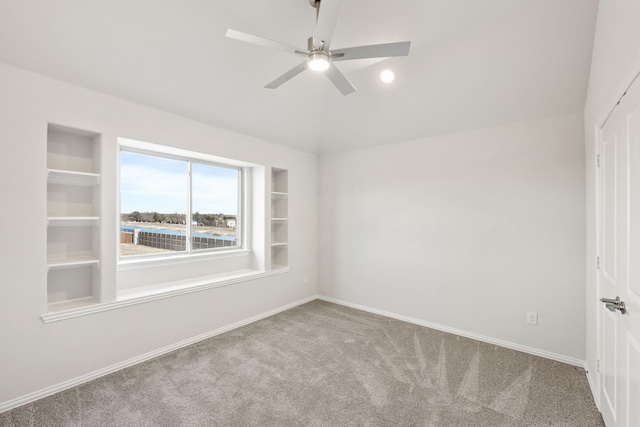 spare room with lofted ceiling, built in features, ceiling fan, a water view, and carpet