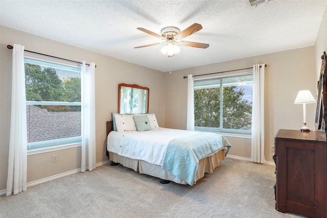 bedroom featuring a textured ceiling, light carpet, multiple windows, and ceiling fan