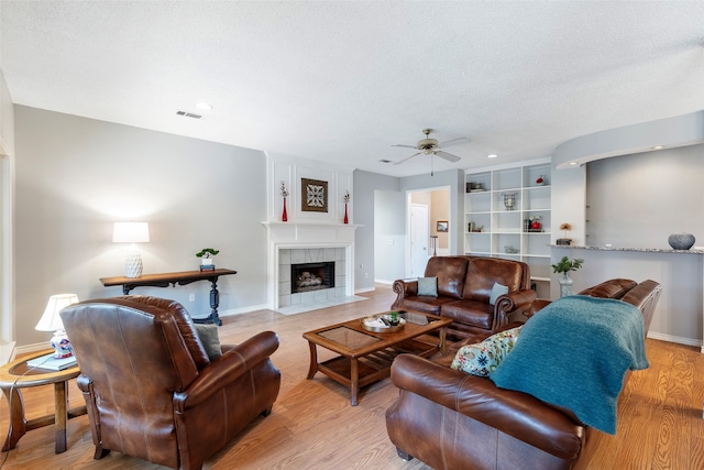 living room featuring a textured ceiling, light hardwood / wood-style flooring, a fireplace, and ceiling fan