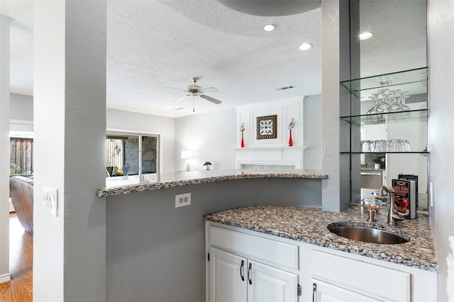 kitchen featuring white cabinets, a textured ceiling, light hardwood / wood-style flooring, dark stone countertops, and sink