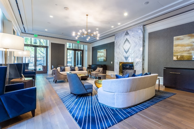 living room with wood-type flooring, crown molding, an inviting chandelier, and a premium fireplace