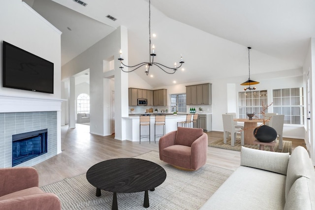 living room with a fireplace, light wood-type flooring, high vaulted ceiling, and an inviting chandelier