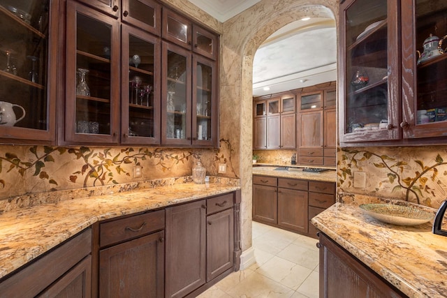 bar with dark brown cabinetry, light stone countertops, ornamental molding, and tasteful backsplash