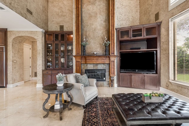 living room featuring a tiled fireplace, crown molding, and a towering ceiling